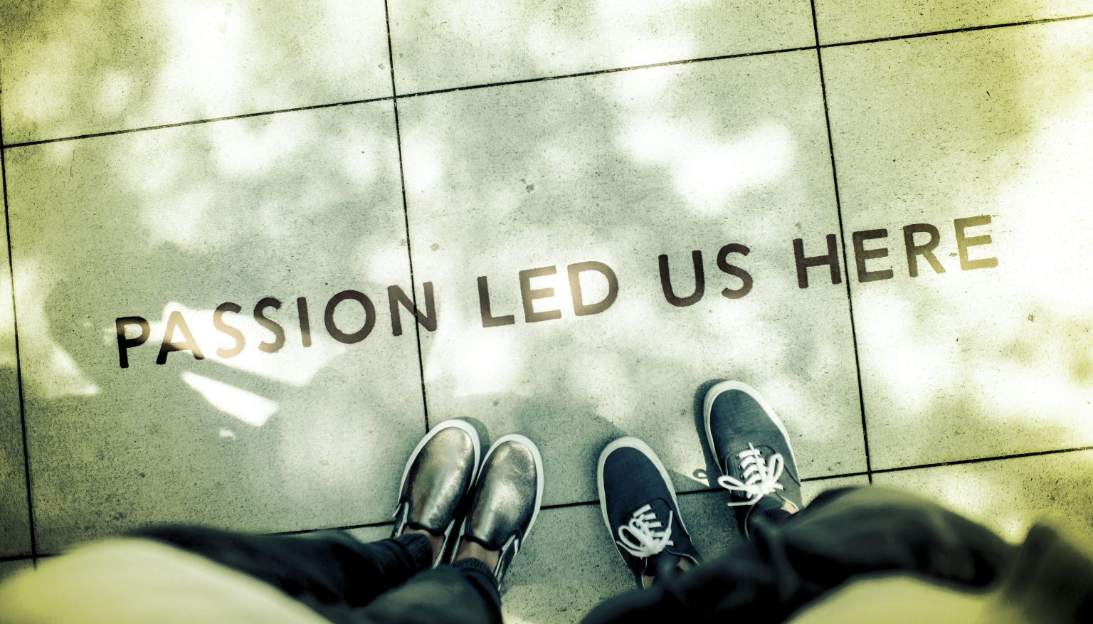 POV: looking down at sidewalk, the words passion led us here" and two sets of feet.